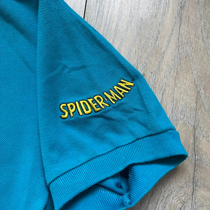 Marvel Comics Spider-Man 1994 Blue Embroidered Polo is a blue polo shirt featuring embroidered Spider-Man branding. The left chest displays an embroidered Spider-Man graphic, while the sleeve includes yellow “Spider-Man” text embroidery. The lower front is finished with small black “1994” text, and the shirt includes a large Marvel Comics neck tag.