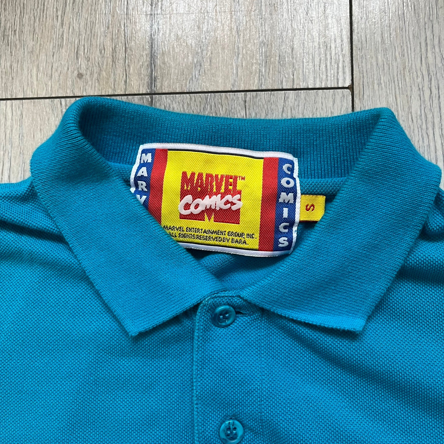 Marvel Comics Spider-Man 1994 Blue Embroidered Polo is a blue polo shirt featuring embroidered Spider-Man branding. The left chest displays an embroidered Spider-Man graphic, while the sleeve includes yellow “Spider-Man” text embroidery. The lower front is finished with small black “1994” text, and the shirt includes a large Marvel Comics neck tag.