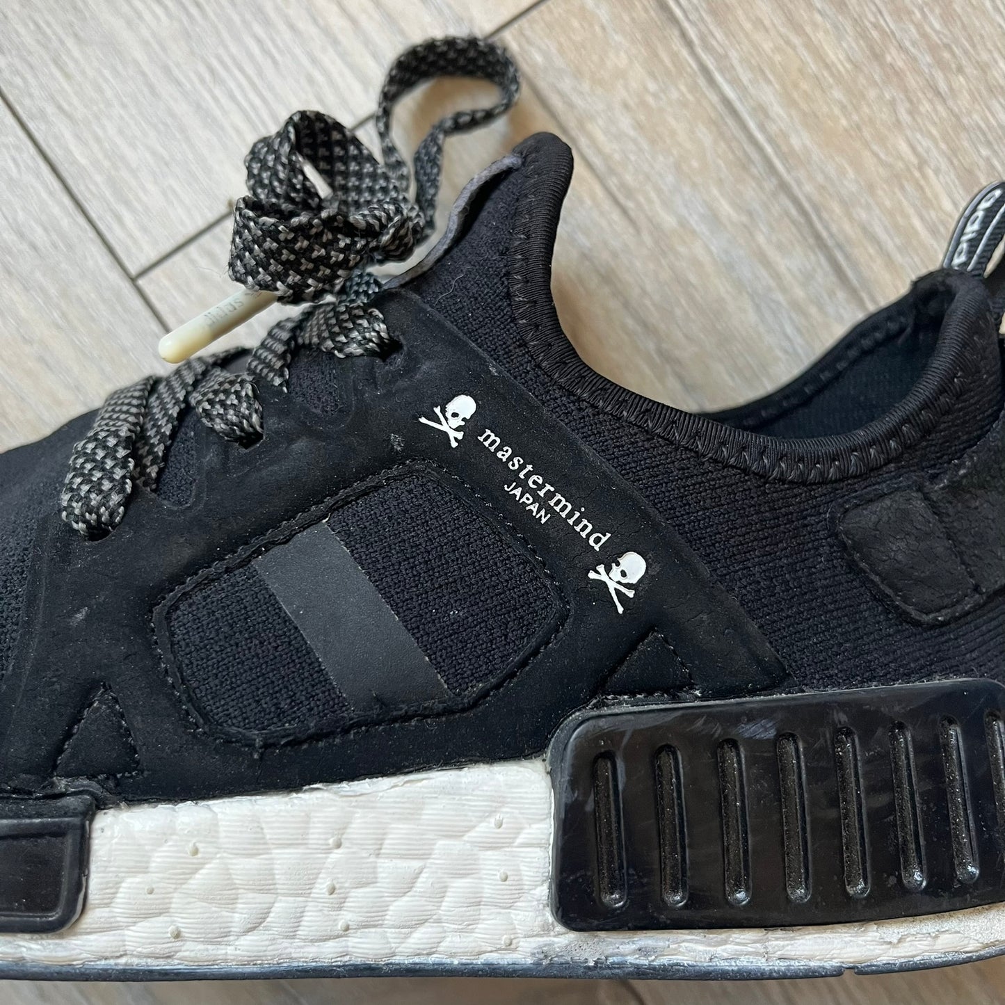 Mastermind x adidas NMD XR1 “Mastermind” Sneakers BA9726 are a 2016 collaboration between adidas and Mastermind Japan, the Japanese label founded by Masaaki Homma. The sneaker features a Core Black/Core Black/White colorway with a polyester mesh upper, rubber sole, and adidas Boost midsole. Mastermind’s signature skull and crossbones logo appears on the leather cage and tongue, while the pair includes black laces and follows the NMD XR1 silhouette released on September 20, 2016 under style code BA9726