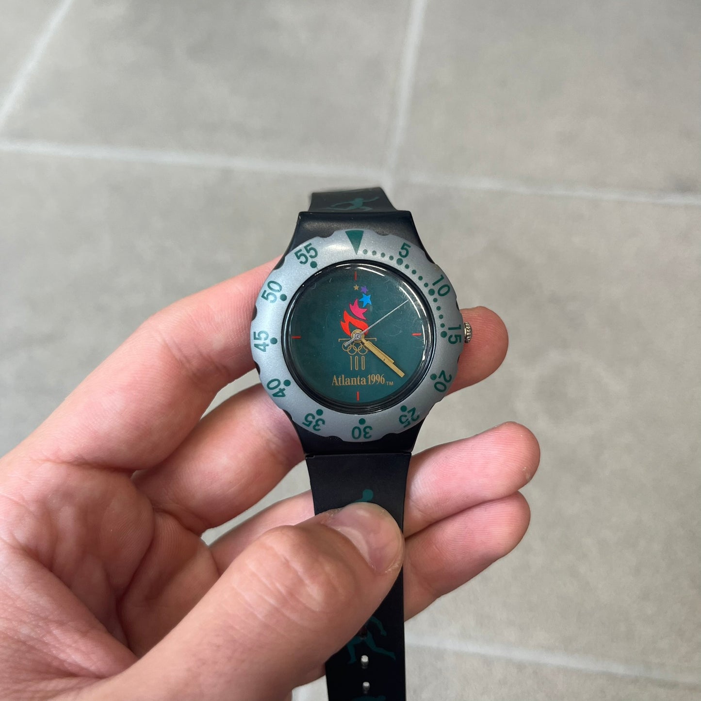 McDonald's 1996 Atlanta Olympics Analog Watch features a black strap decorated with green sports-themed figures and a silver and grey case. The green dial has the Atlanta 1996 Olympic Games logo at the center. A vintage McDonald's promotional watch from the 1996 Atlanta Olympics.
