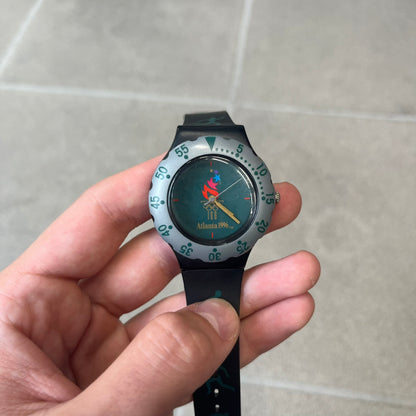 McDonald's 1996 Atlanta Olympics Analog Watch features a black strap decorated with green sports-themed figures and a silver and grey case. The green dial has the Atlanta 1996 Olympic Games logo at the center. A vintage McDonald's promotional watch from the 1996 Atlanta Olympics.
