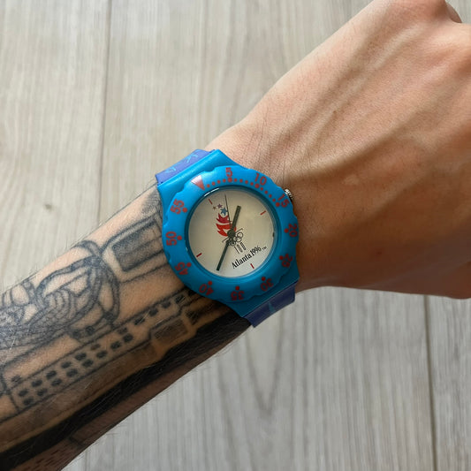 McDonald’s Atlanta 1996 Olympics analog watch with a dark blue strap featuring light blue sport-themed motifs. The dial is white with blue and red accents, showcasing the official Atlanta 1996 logo. A nostalgic collectible celebrating the iconic Olympic collaboration.