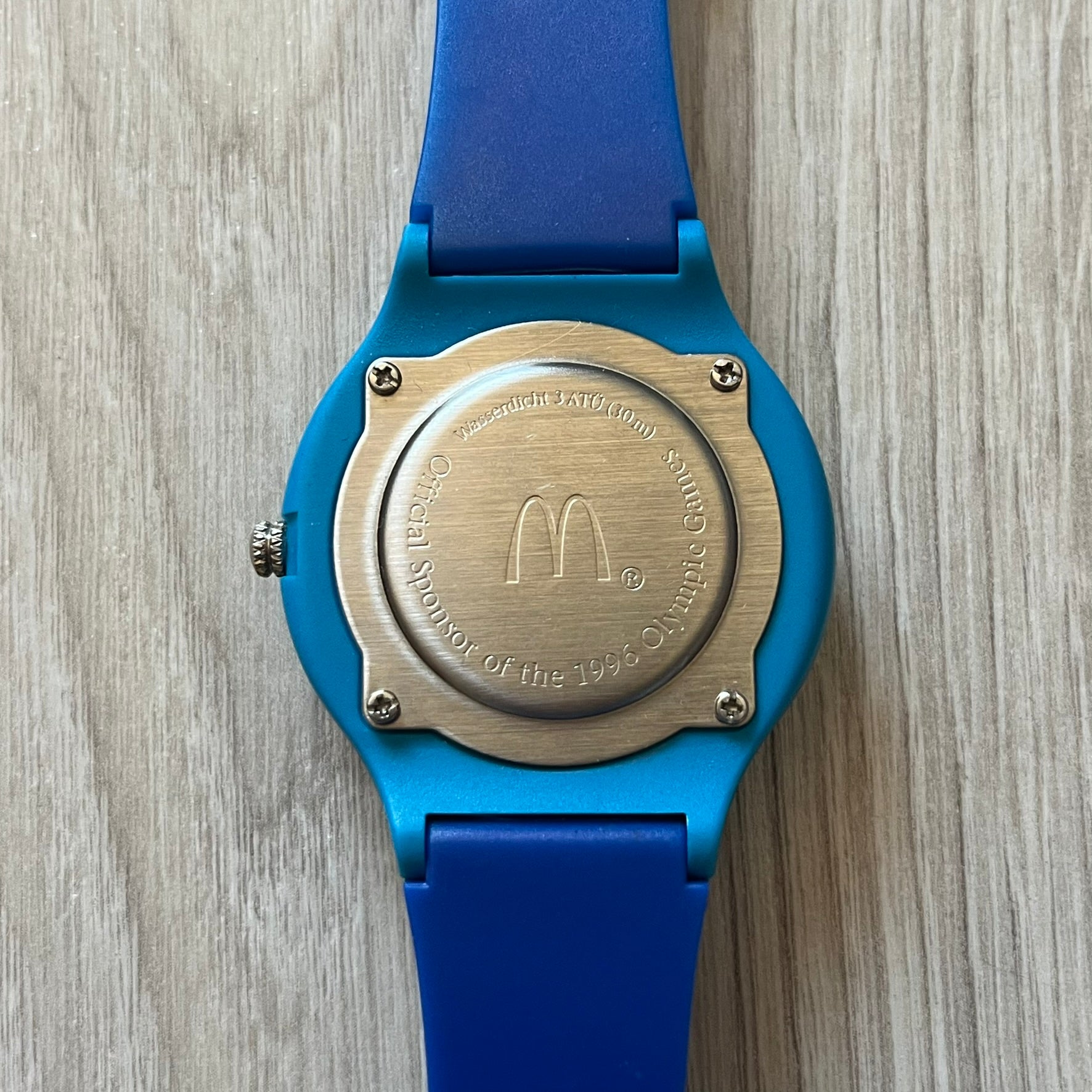 McDonald’s Atlanta 1996 Olympics analog watch with a dark blue strap featuring light blue sport-themed motifs. The dial is white with blue and red accents, showcasing the official Atlanta 1996 logo. A nostalgic collectible celebrating the iconic Olympic collaboration.