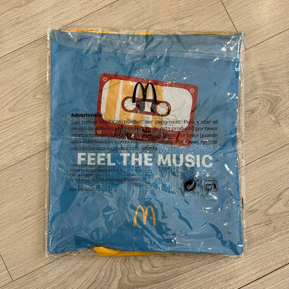 The McDonald’s Spain “Feel The Music” Backpack comes in a blue and yellow colorway with a vintage cassette graphic on the front. Constructed from lightweight non-woven synthetic fabric, it includes yellow straps and a zip-top closure. A collectible promotional item released by McDonald’s Spain.