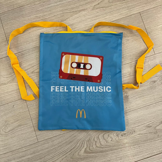 The McDonald’s Spain “Feel The Music” Backpack comes in a blue and yellow colorway with a vintage cassette graphic on the front. Constructed from lightweight non-woven synthetic fabric, it includes yellow straps and a zip-top closure. A collectible promotional item released by McDonald’s Spain.