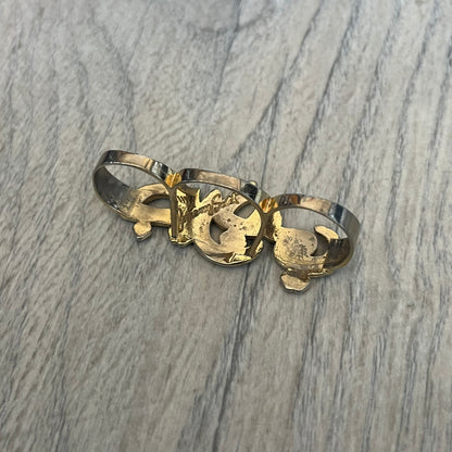Melody Ehsani x Jeremy Scott 2013 Arabic Three Finger Ring is a gold-tone three-finger ring from the 2013 Fearless collection by Melody Ehsani and Jeremy Scott. The ring features the name “Jeremy” written in Arabic script across the three connected bands. Released in 2013, the piece originally retailed for $100.