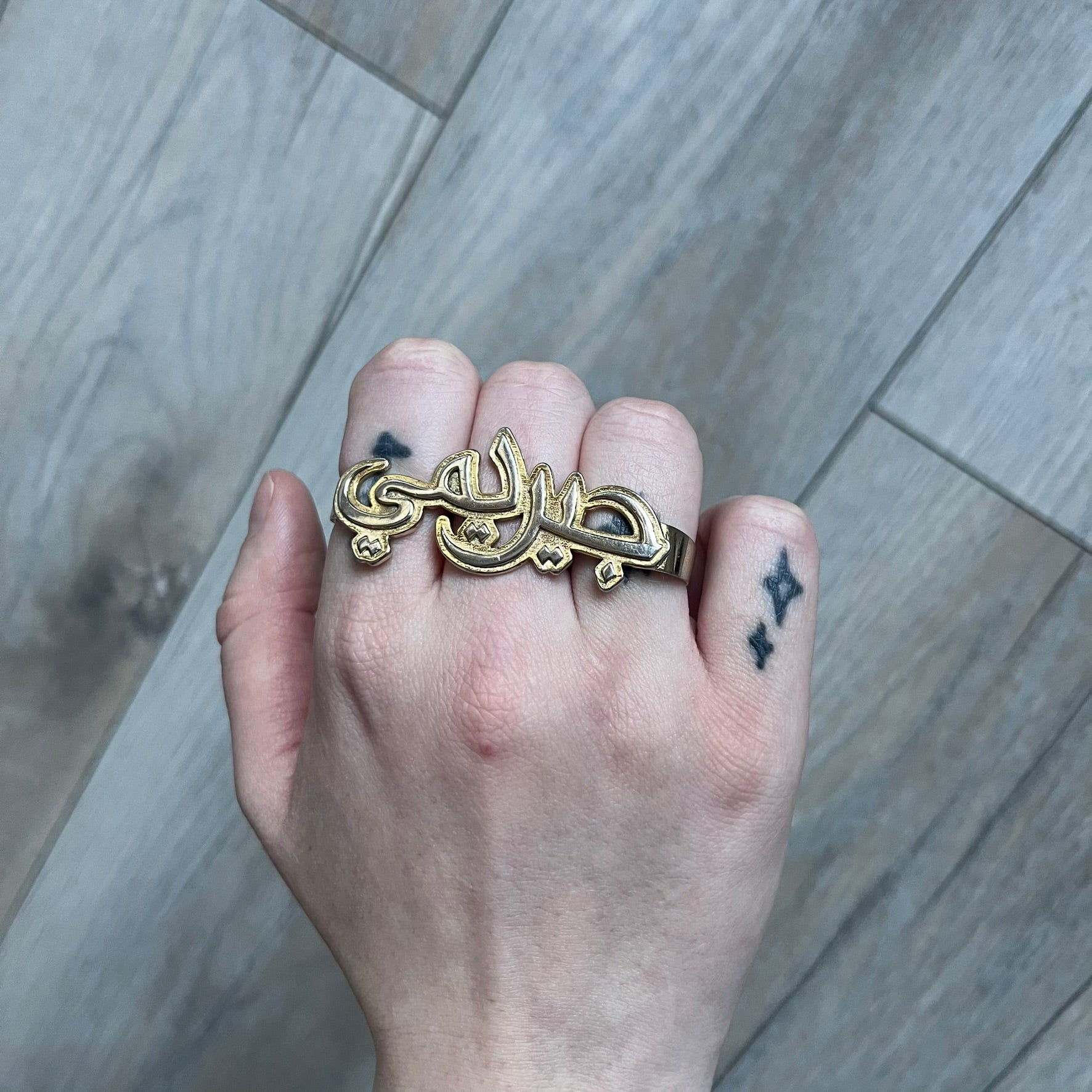 Melody Ehsani x Jeremy Scott 2013 Arabic Three Finger Ring is a gold-tone three-finger ring from the 2013 Fearless collection by Melody Ehsani and Jeremy Scott. The ring features the name “Jeremy” written in Arabic script across the three connected bands. Released in 2013, the piece originally retailed for $100.