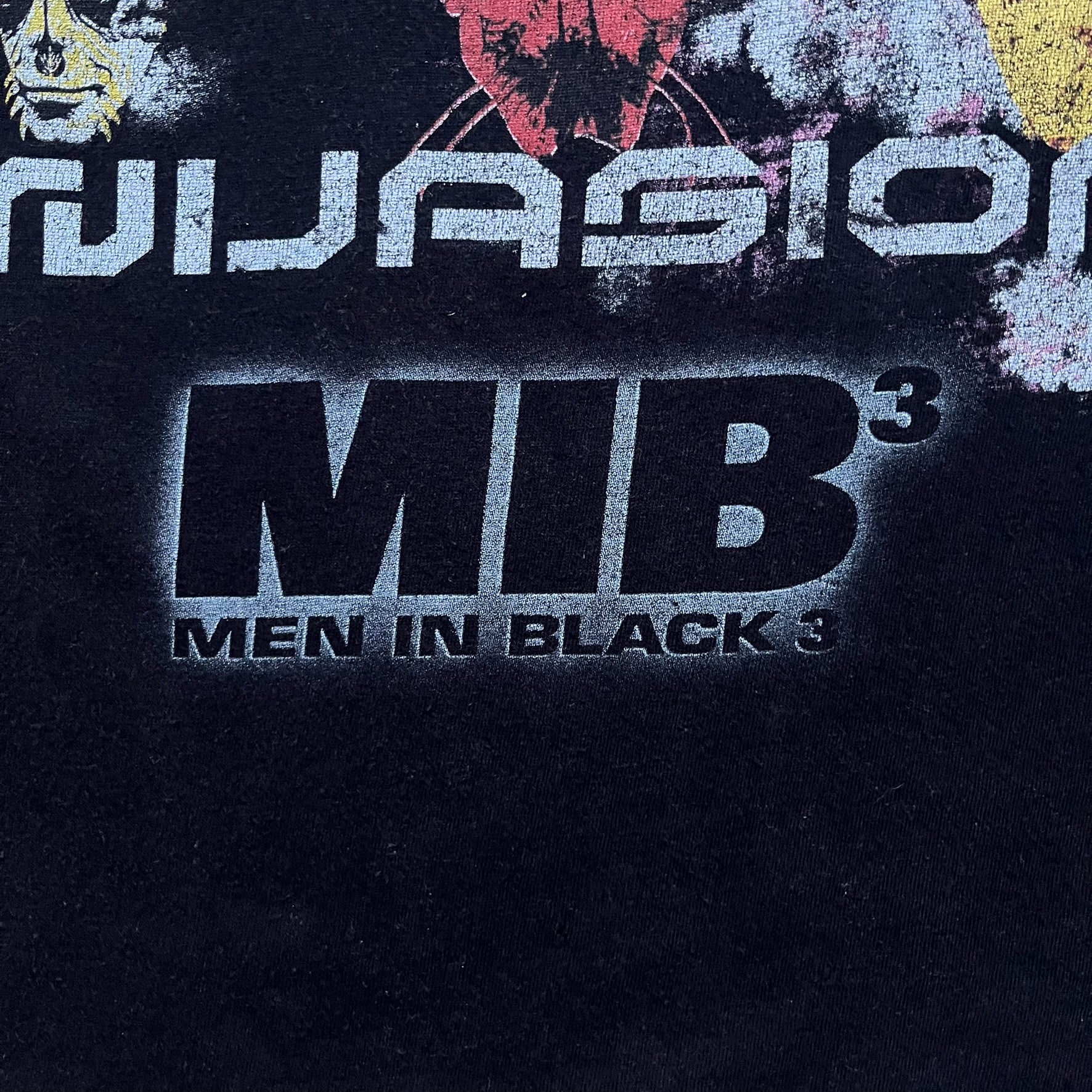 Black Men In Black 3 T-shirt from 2012, featuring a front graphic with nine colorful alien faces arranged in a 3×3 grid. The phrase “It’s a Full Scale Invasion” is printed between the faces, with a white Men In Black 3 logo placed below. Finished with an official MIB neck tag, short sleeves, and a standard crew neckline.