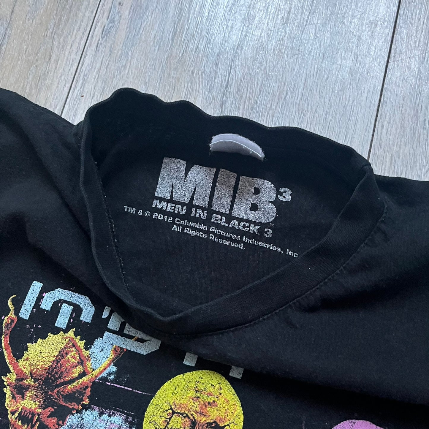 Black Men In Black 3 T-shirt from 2012, featuring a front graphic with nine colorful alien faces arranged in a 3×3 grid. The phrase “It’s a Full Scale Invasion” is printed between the faces, with a white Men In Black 3 logo placed below. Finished with an official MIB neck tag, short sleeves, and a standard crew neckline.