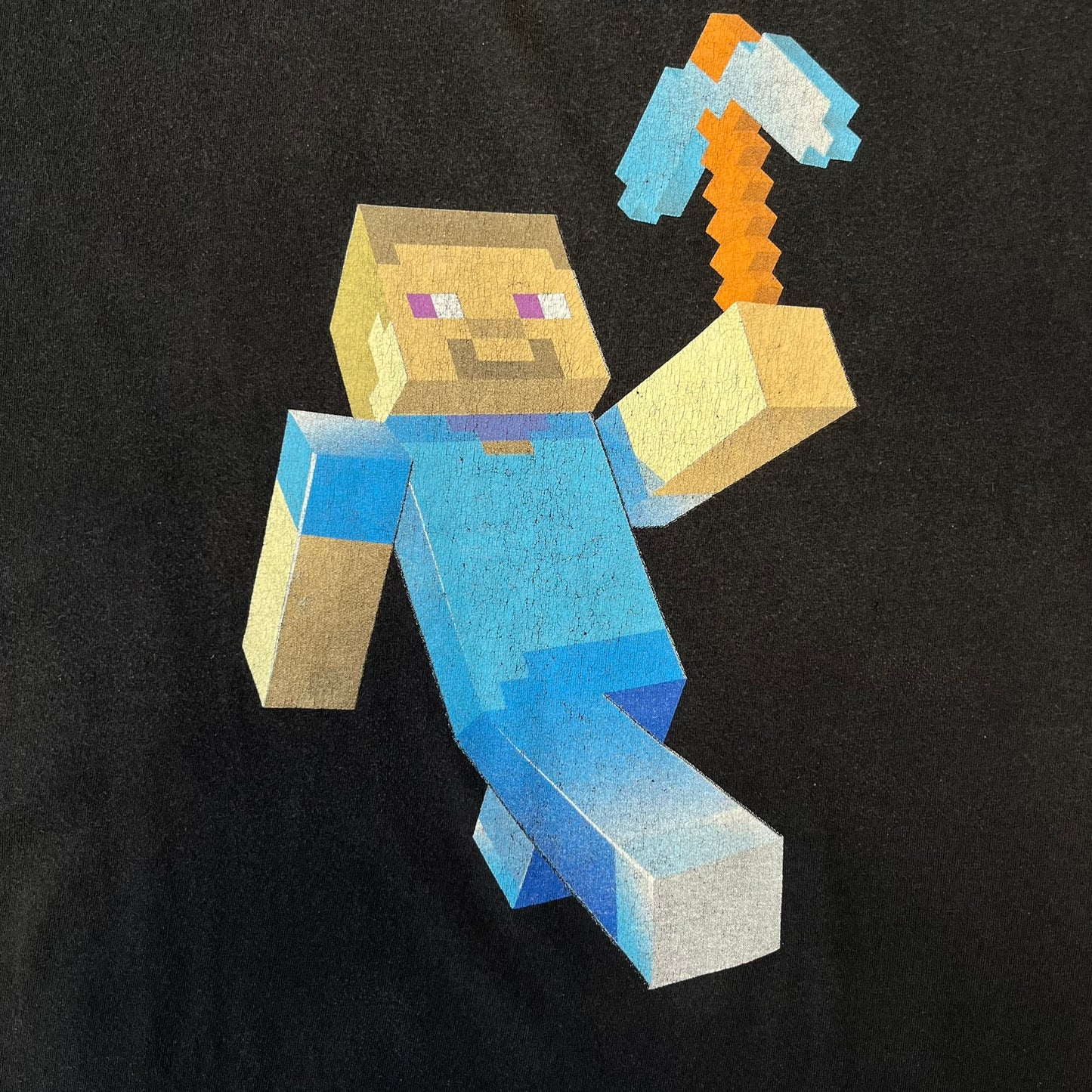 Minecraft 2012 Xbox 360 Black Promo Tee features a black design with Steve from Minecraft walking while holding a diamond pickaxe on the front. The sleeve has a white Xbox 360 logo, while the back features three white gaming-related logos including Mojang. A promotional release from 2012.
