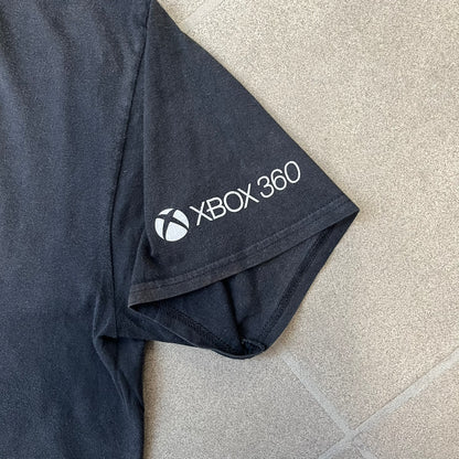 Minecraft 2012 Xbox 360 Black Promo Tee features a black design with Steve from Minecraft walking while holding a diamond pickaxe on the front. The sleeve has a white Xbox 360 logo, while the back features three white gaming-related logos including Mojang. A promotional release from 2012.
