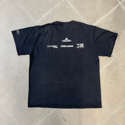 Minecraft 2012 Xbox 360 Black Promo Tee features a black design with Steve from Minecraft walking while holding a diamond pickaxe on the front. The sleeve has a white Xbox 360 logo, while the back features three white gaming-related logos including Mojang. A promotional release from 2012.
