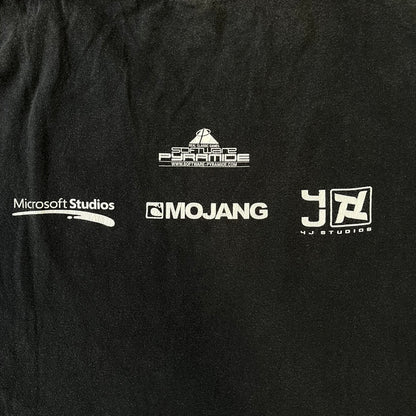 Minecraft 2012 Xbox 360 Black Promo Tee features a black design with Steve from Minecraft walking while holding a diamond pickaxe on the front. The sleeve has a white Xbox 360 logo, while the back features three white gaming-related logos including Mojang. A promotional release from 2012.
