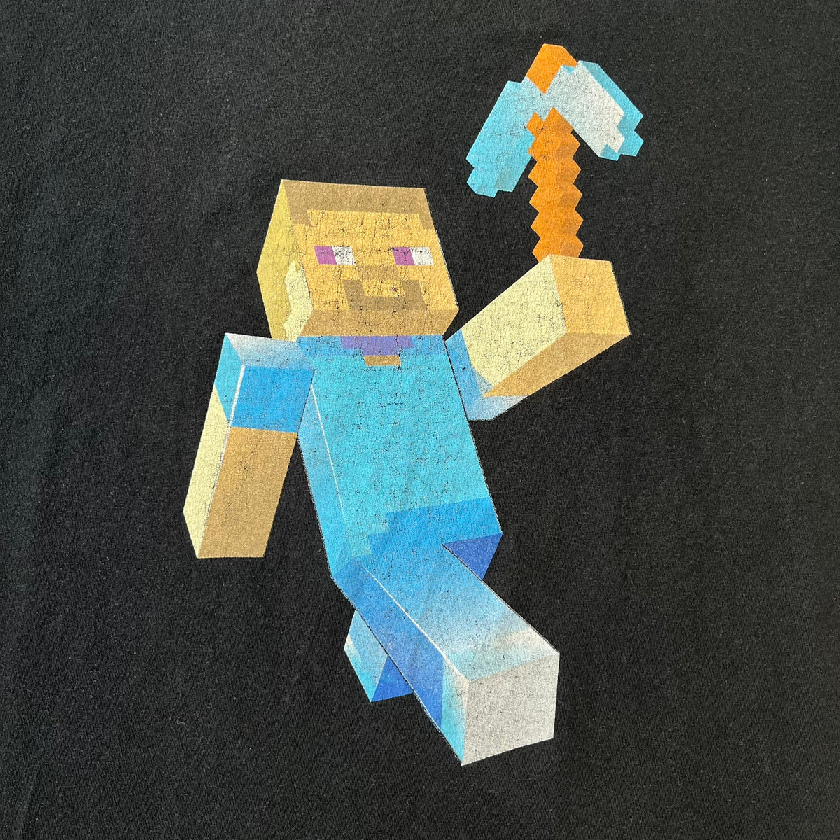 Minecraft 2012 Xbox 360 Black Promo Tee features a black design with Steve from Minecraft walking while holding a diamond pickaxe on the front. The sleeve has a white Xbox 360 logo, while the back features three white gaming-related logos including Mojang. A promotional release from 2012.
