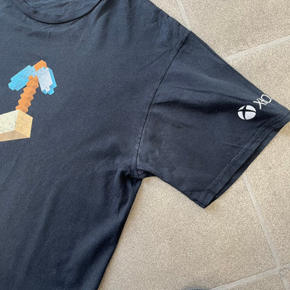 Minecraft 2012 Xbox 360 Black Promo Tee features a black design with Steve from Minecraft walking while holding a diamond pickaxe on the front. The sleeve has a white Xbox 360 logo, while the back features three white gaming-related logos including Mojang. A promotional release from 2012.
