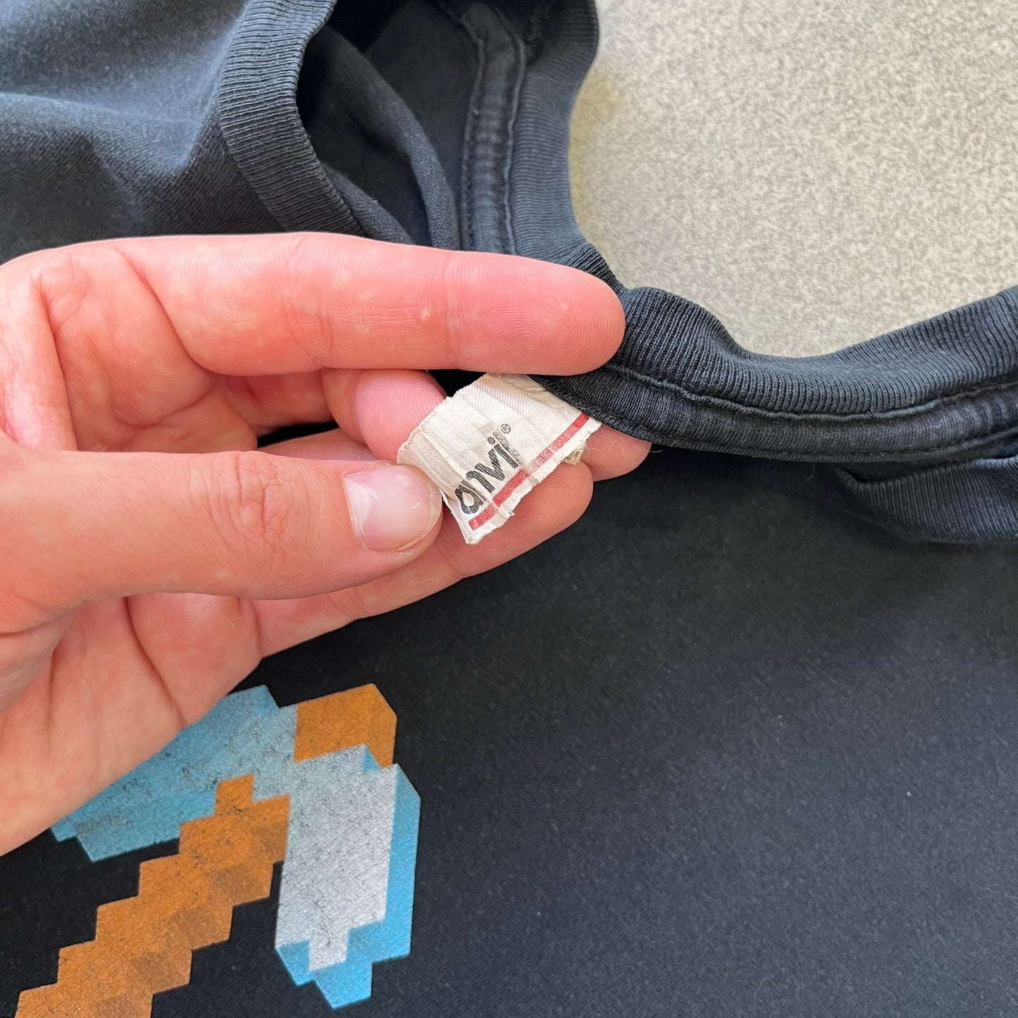 Minecraft 2012 Xbox 360 Black Promo Tee features a black design with Steve from Minecraft walking while holding a diamond pickaxe on the front. The sleeve has a white Xbox 360 logo, while the back features three white gaming-related logos including Mojang. A promotional release from 2012.
