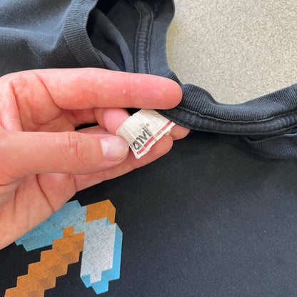 Minecraft 2012 Xbox 360 Black Promo Tee features a black design with Steve from Minecraft walking while holding a diamond pickaxe on the front. The sleeve has a white Xbox 360 logo, while the back features three white gaming-related logos including Mojang. A promotional release from 2012.
