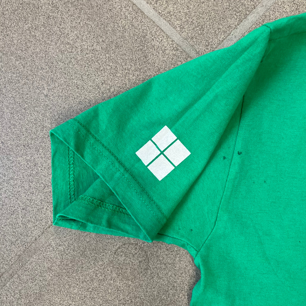 Minecraft 2015 Minecon London Green Tee is a green T-shirt made for Minecon 2015 in London, featuring Big Ben with a Creeper face on the front, with “Minecon London July 4-5” text in Minecraft-style lettering. The upper back displays “Minecon” with “Thanks for Playing” text below, while the sleeves carry a Mojang logo on one side and a Microsoft logo on the other.