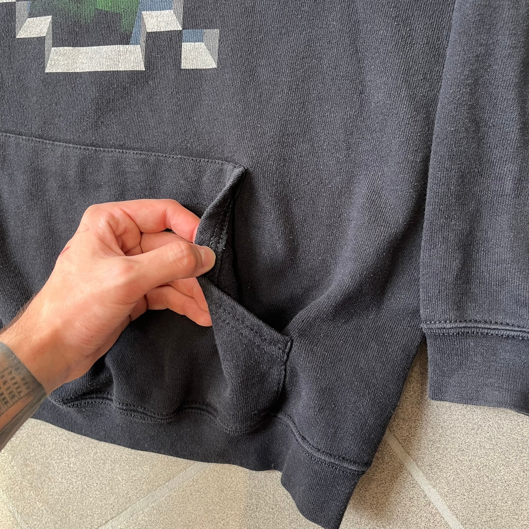 Minecraft Creeper 2013 J!NX Hoodie is a black 80/20 cotton-poly blend hoodie produced by Mojang and J!NX. The front features a Creeper graphic peeking through a pixelated hole designed to resemble in-game Minecraft blocks. This piece was released in 2013 as official Minecraft merchandise.