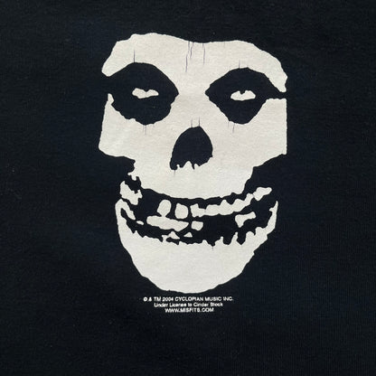 Misfits 2004 Fiend Skull Black Tee is a black T-shirt made in the USA on an American Apparel Classic Girl blank. The front features the band’s white Fiend Skull graphic printed on the chest. The shirt includes 2004 Cyclopian Music Inc. licensing and a Misfits neck tag.