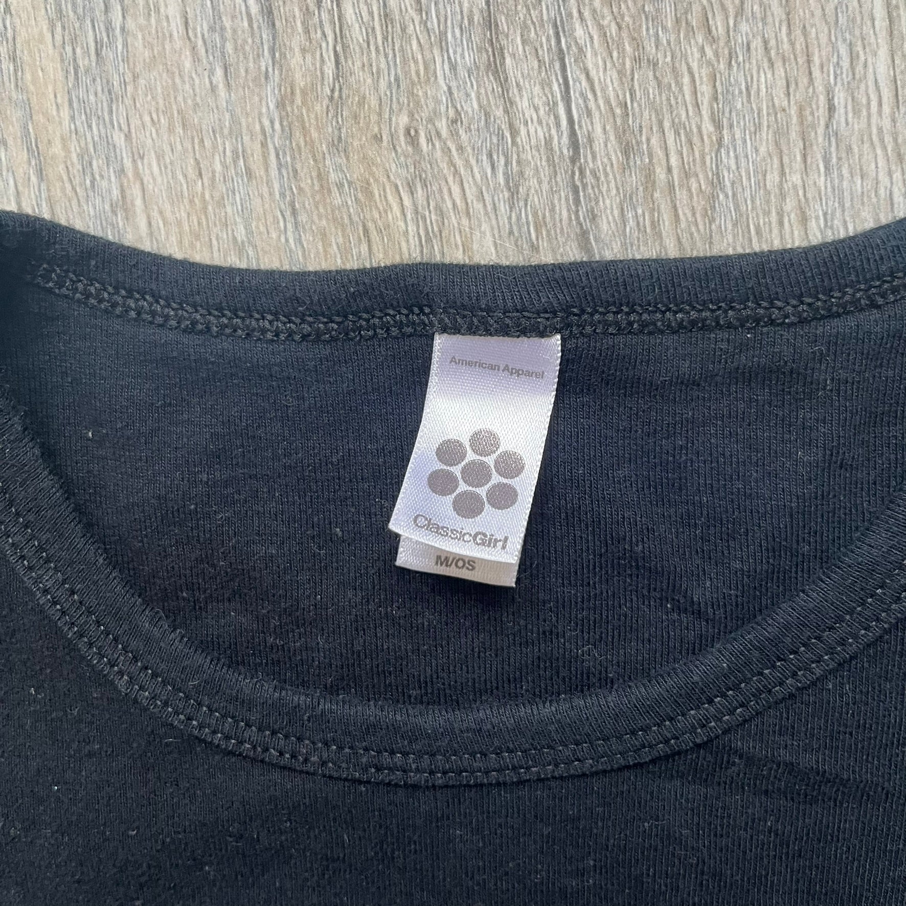 Misfits 2004 Fiend Skull Black Tee is a black T-shirt made in the USA on an American Apparel Classic Girl blank. The front features the band’s white Fiend Skull graphic printed on the chest. The shirt includes 2004 Cyclopian Music Inc. licensing and a Misfits neck tag.