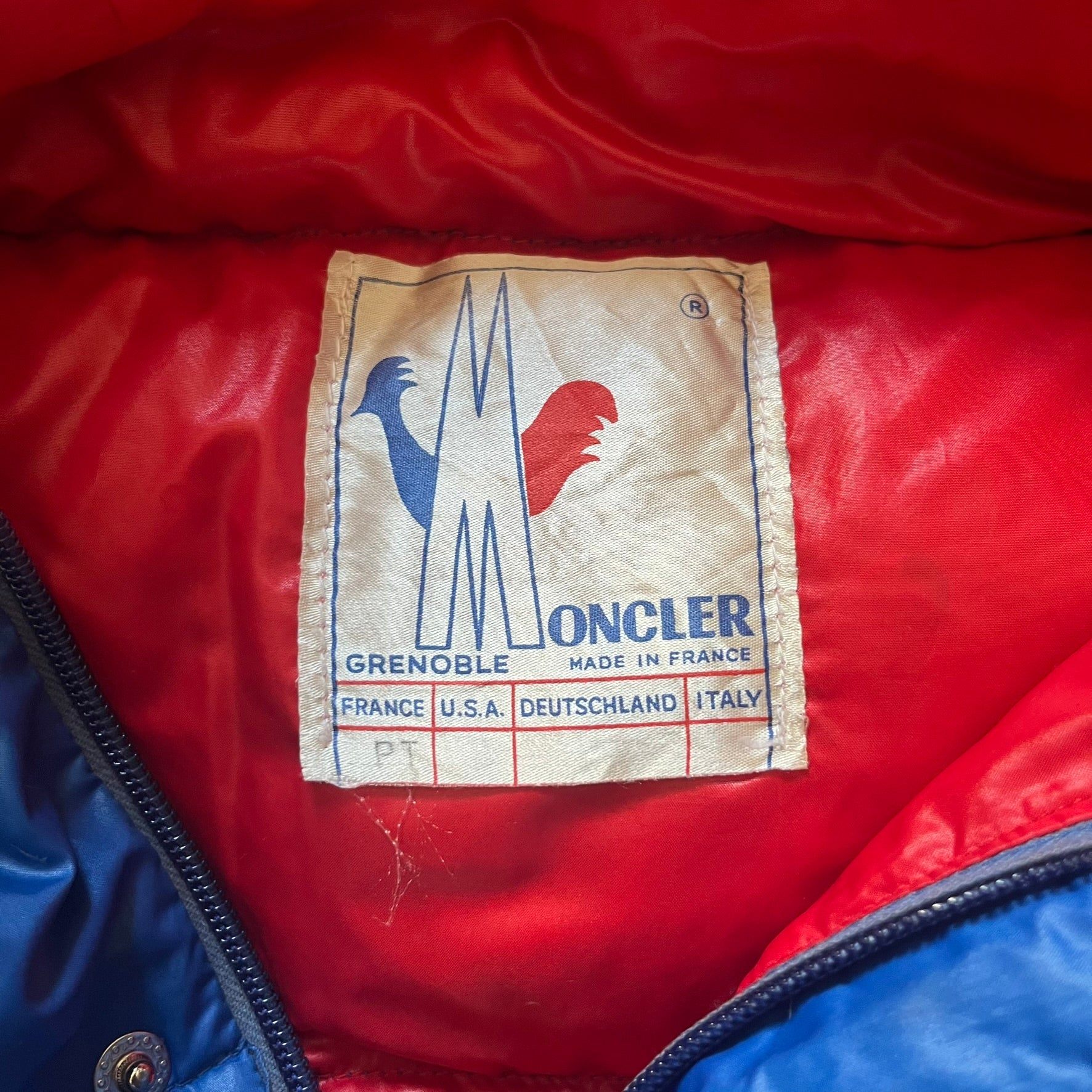 Vintage 1980s Moncler Grenoble down jacket in blue with a contrasting red lining. Features a foldable thin hood hidden in the back, silver-tone buttons and zippers, and the original Moncler patch on the sleeve. A rare French-made piece with authentic Grenoble labels, distinct from the brand’s modern ski line.