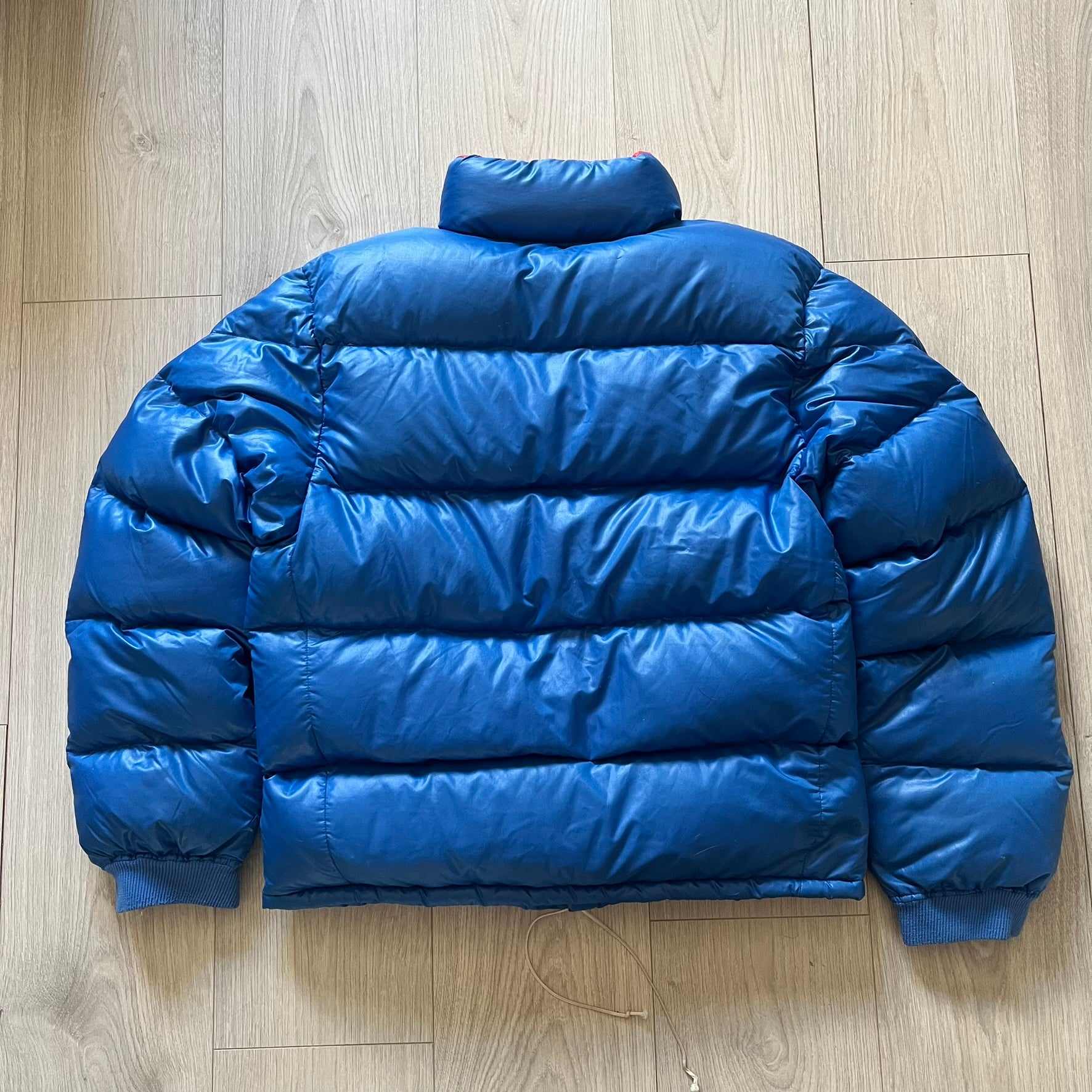 Vintage 1980s Moncler Grenoble down jacket in blue with a contrasting red lining. Features a foldable thin hood hidden in the back, silver-tone buttons and zippers, and the original Moncler patch on the sleeve. A rare French-made piece with authentic Grenoble labels, distinct from the brand’s modern ski line.