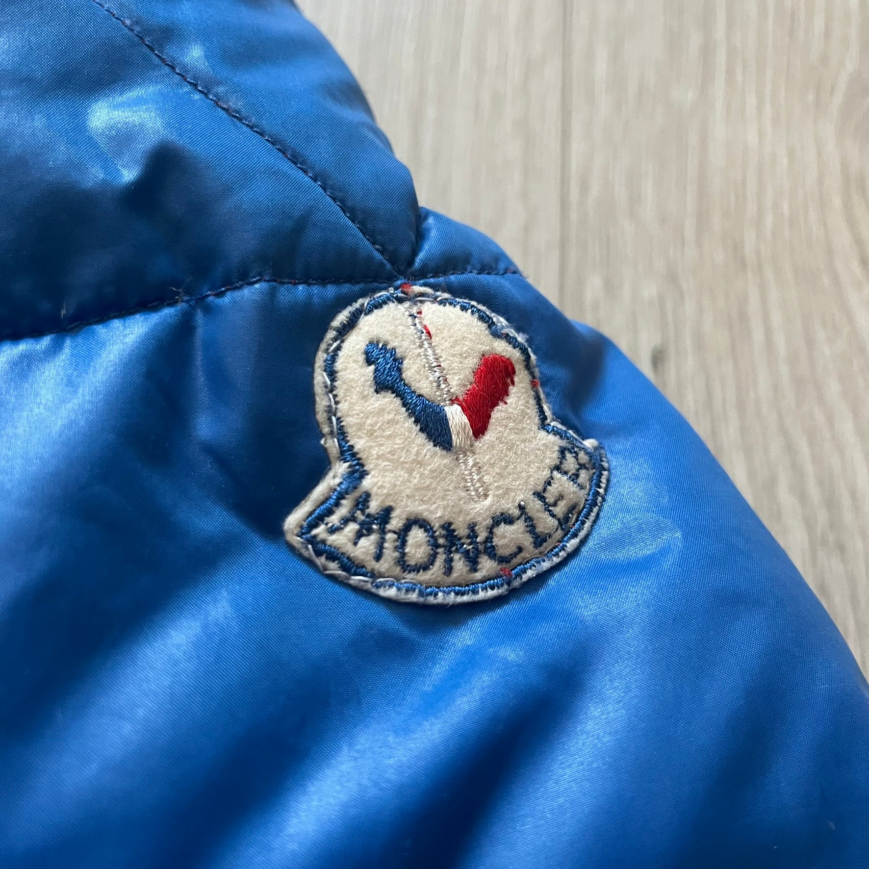 Vintage 1980s Moncler Grenoble down jacket in blue with a contrasting red lining. Features a foldable thin hood hidden in the back, silver-tone buttons and zippers, and the original Moncler patch on the sleeve. A rare French-made piece with authentic Grenoble labels, distinct from the brand’s modern ski line.