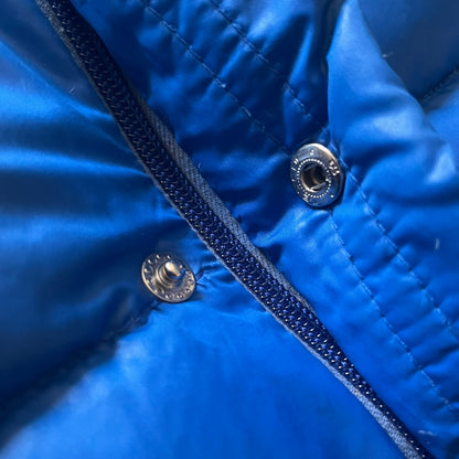 Vintage 1980s Moncler Grenoble down jacket in blue with a contrasting red lining. Features a foldable thin hood hidden in the back, silver-tone buttons and zippers, and the original Moncler patch on the sleeve. A rare French-made piece with authentic Grenoble labels, distinct from the brand’s modern ski line.