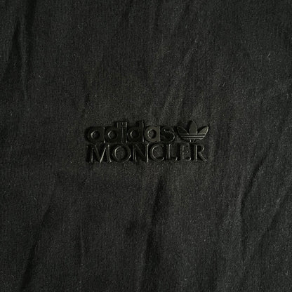 Moncler x Adidas Originals Longsleeve from the FW23 collection. Crafted in cotton jersey, the piece features a three-panel color-block design transitioning from beige to black tones. It includes a silicone chest logo, black Adidas stripes down the sleeves, and a co-branded Moncler x Adidas logo patch on the arm.