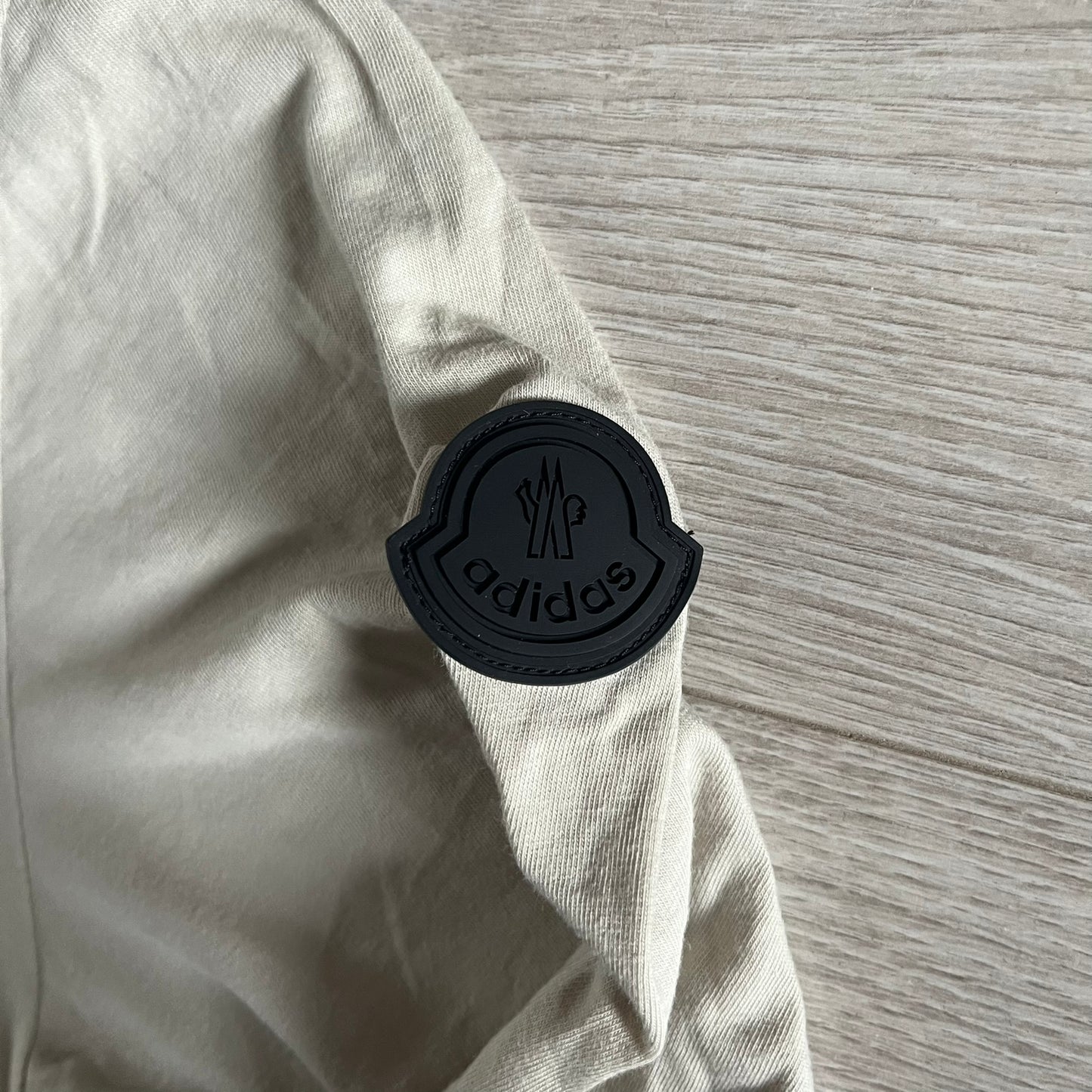 Moncler x Adidas Originals Longsleeve from the FW23 collection. Crafted in cotton jersey, the piece features a three-panel color-block design transitioning from beige to black tones. It includes a silicone chest logo, black Adidas stripes down the sleeves, and a co-branded Moncler x Adidas logo patch on the arm.