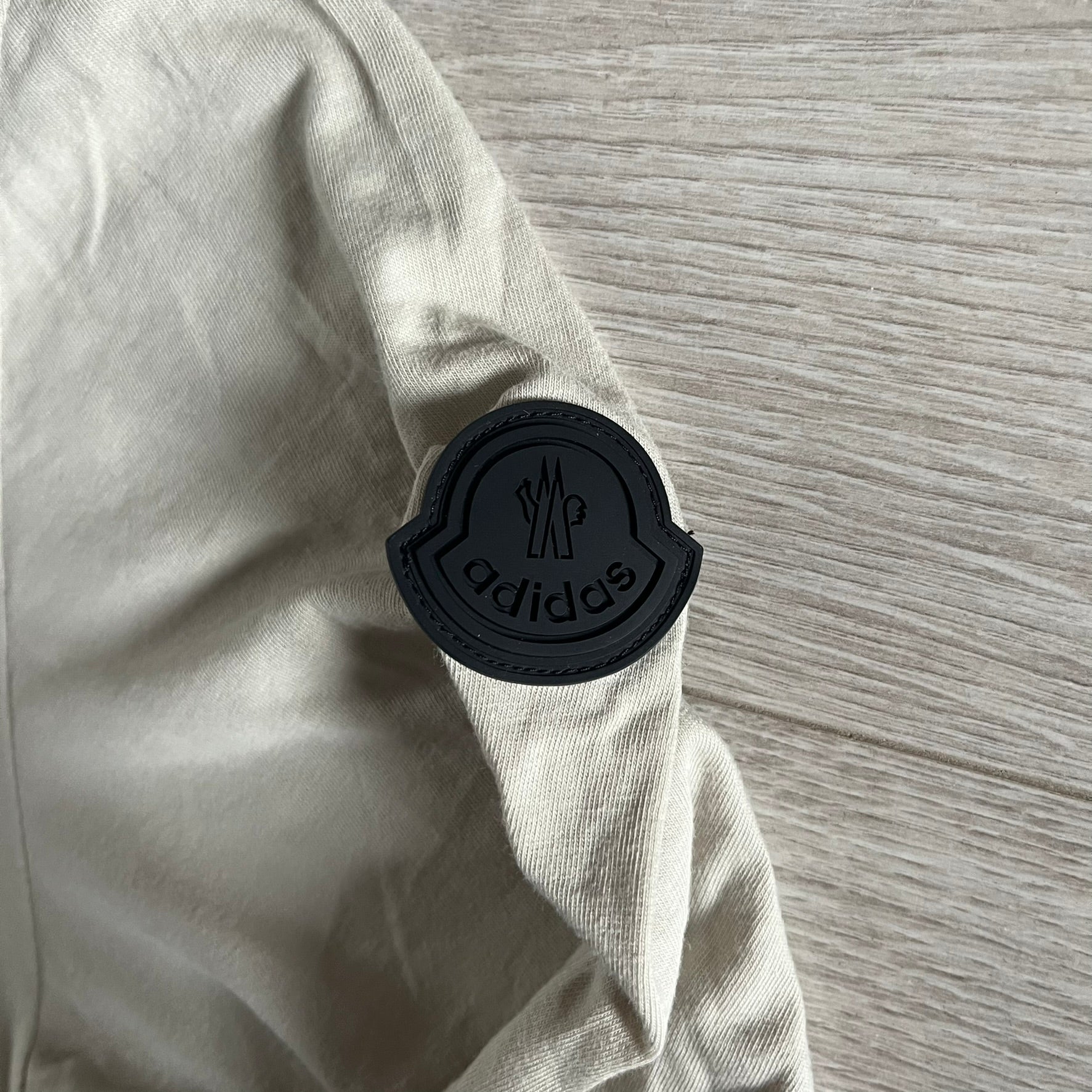 Moncler x Adidas Originals Longsleeve from the FW23 collection. Crafted in cotton jersey, the piece features a three-panel color-block design transitioning from beige to black tones. It includes a silicone chest logo, black Adidas stripes down the sleeves, and a co-branded Moncler x Adidas logo patch on the arm.
