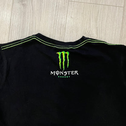 Monster Energy Eyes Tee in black, featuring a graphic of a woman’s eyes with the Monster logo and text on the front in gray and white tones. Green shoulder stitching and a Monster Energy logo on the back under the collar. Made from 95% cotton and 5% Lycra.