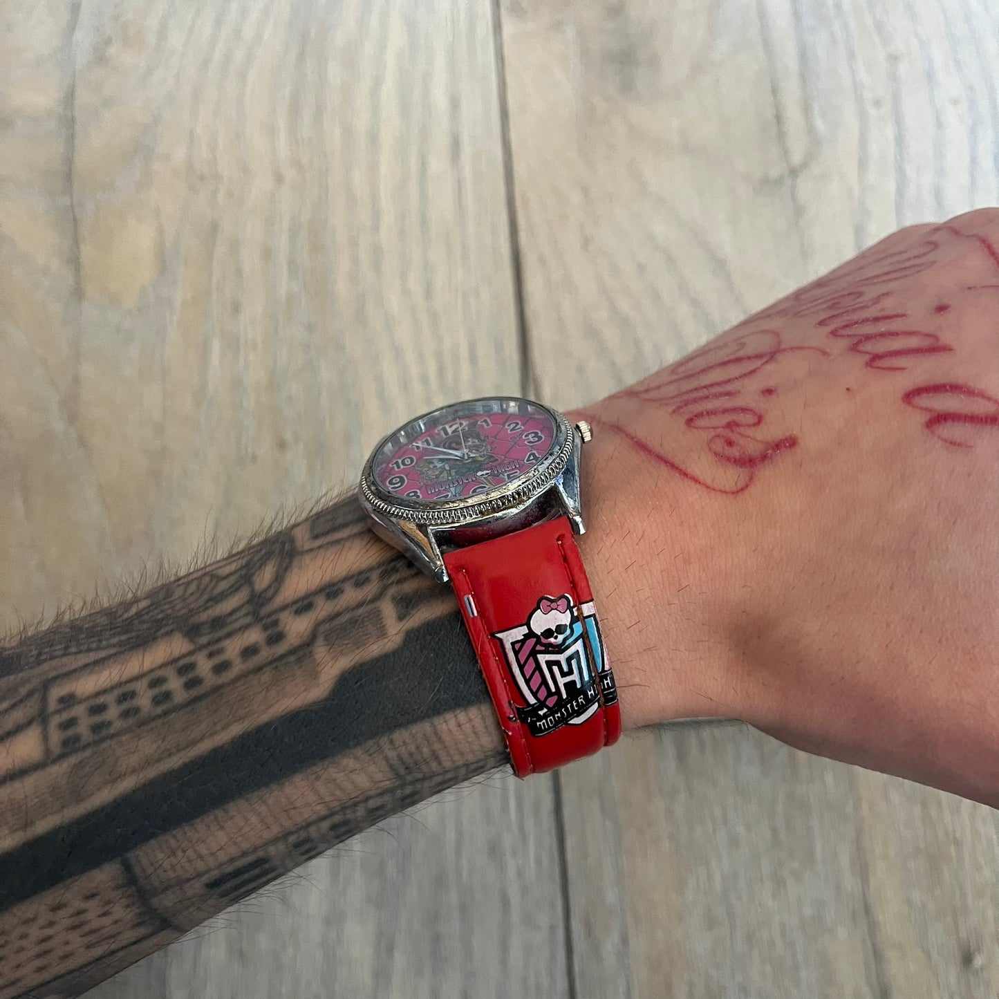 Monster High Red & Pink Kids Watch is a children’s wristwatch featuring a red strap printed with Monster High logos and character graphics. The watch has a silver-tone case with a pink dial, black numerals, and white hands, along with a Monster High character graphic and logo on the face. It comes packaged in a pink box with full Monster High branding.