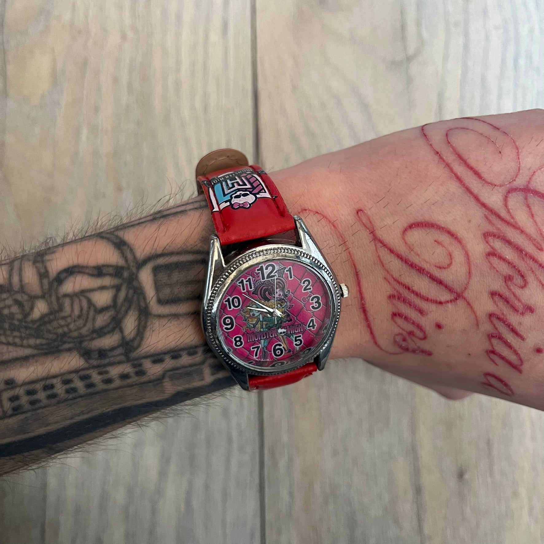 Monster High Red & Pink Kids Watch is a children’s wristwatch featuring a red strap printed with Monster High logos and character graphics. The watch has a silver-tone case with a pink dial, black numerals, and white hands, along with a Monster High character graphic and logo on the face. It comes packaged in a pink box with full Monster High branding.