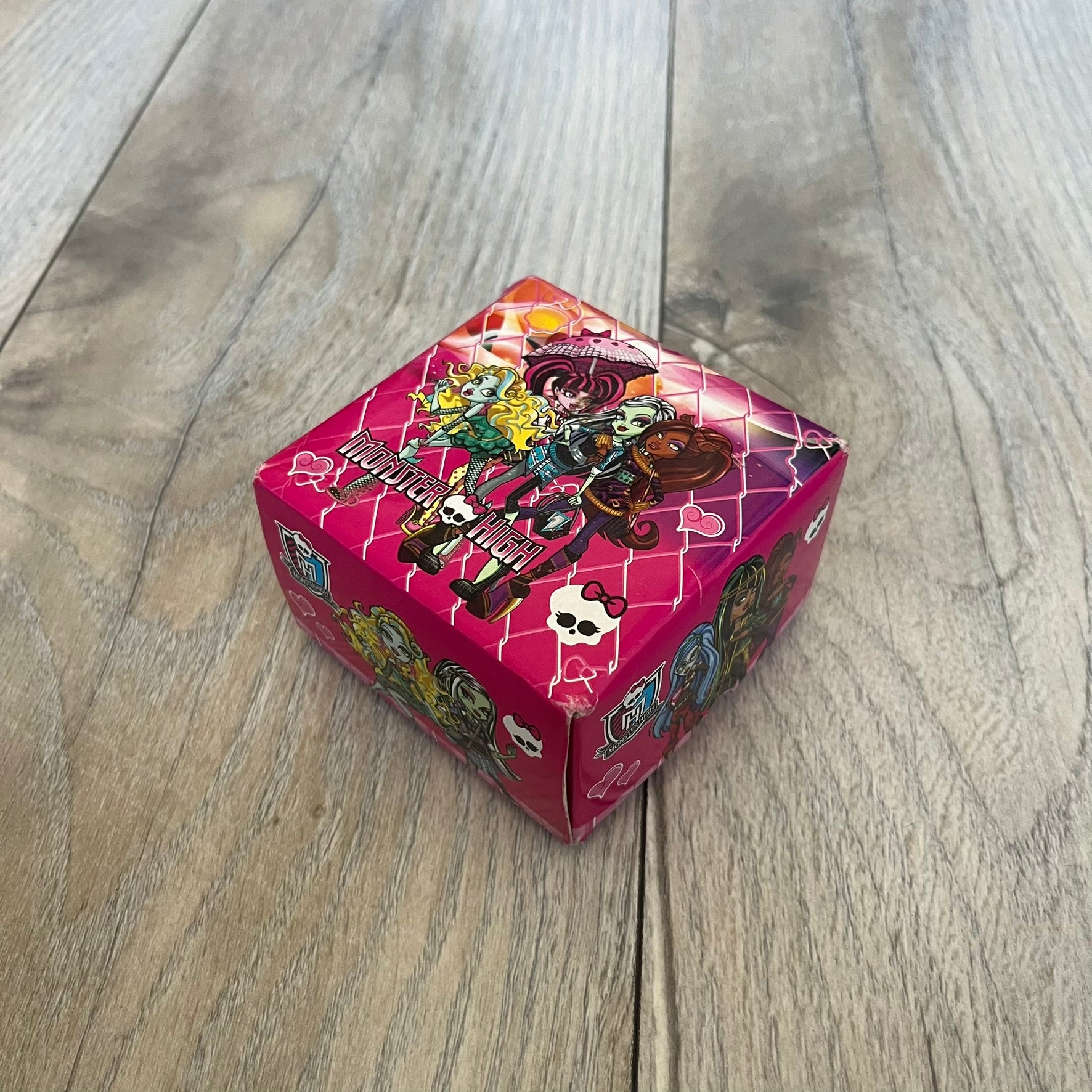 Monster High Red & Pink Kids Watch is a children’s wristwatch featuring a red strap printed with Monster High logos and character graphics. The watch has a silver-tone case with a pink dial, black numerals, and white hands, along with a Monster High character graphic and logo on the face. It comes packaged in a pink box with full Monster High branding.