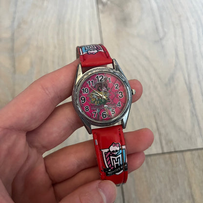 Monster High Red & Pink Kids Watch is a children’s wristwatch featuring a red strap printed with Monster High logos and character graphics. The watch has a silver-tone case with a pink dial, black numerals, and white hands, along with a Monster High character graphic and logo on the face. It comes packaged in a pink box with full Monster High branding.