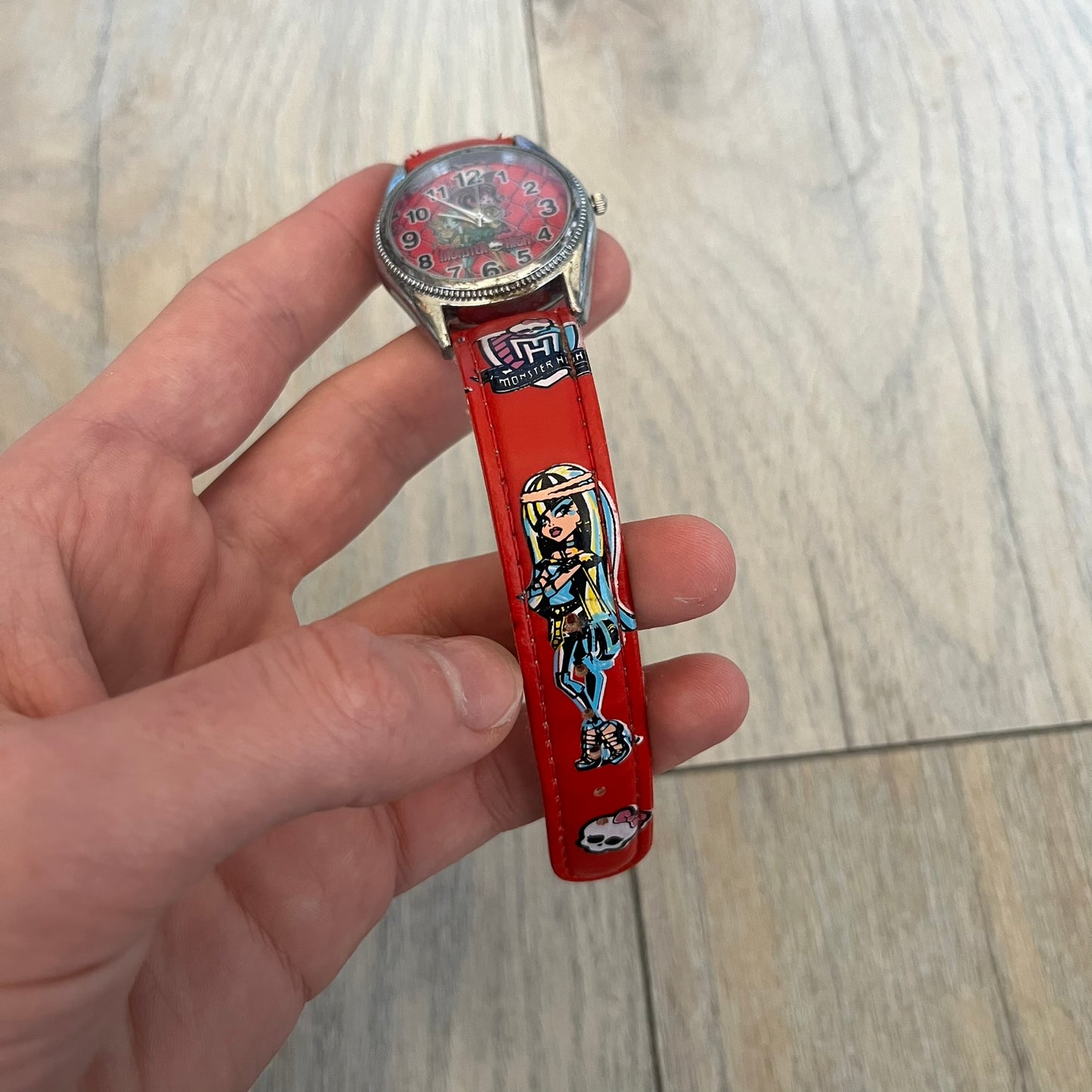 Monster High Red & Pink Kids Watch is a children’s wristwatch featuring a red strap printed with Monster High logos and character graphics. The watch has a silver-tone case with a pink dial, black numerals, and white hands, along with a Monster High character graphic and logo on the face. It comes packaged in a pink box with full Monster High branding.