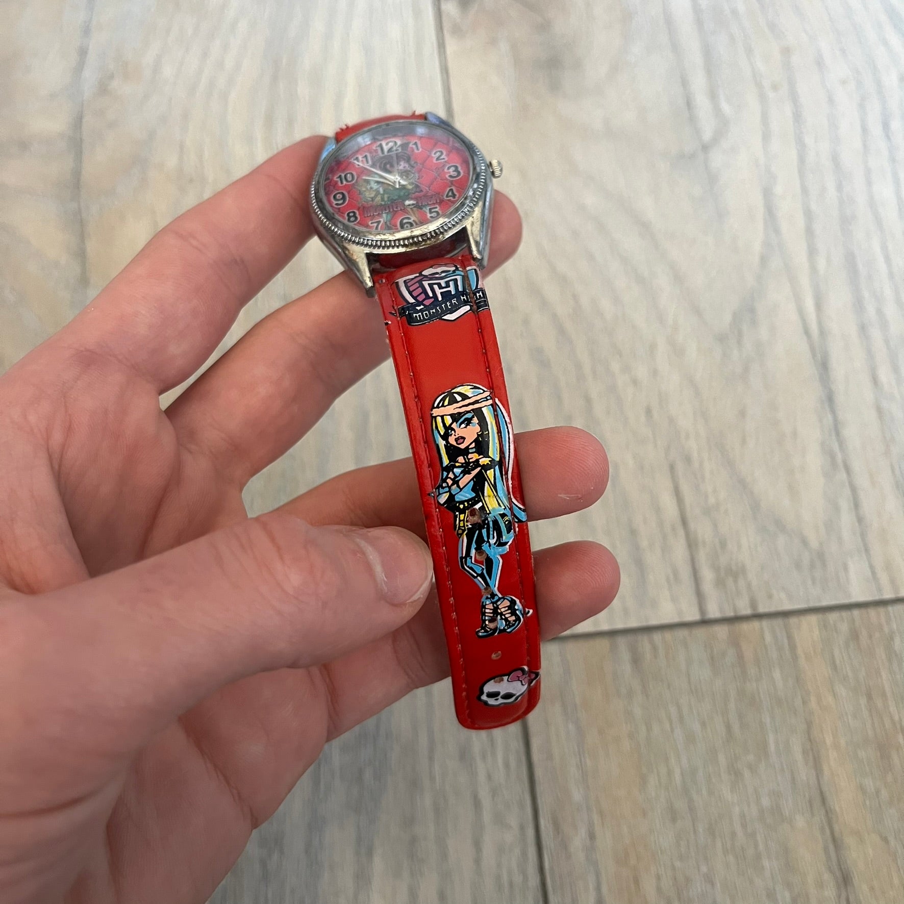 Monster High Red & Pink Kids Watch is a children’s wristwatch featuring a red strap printed with Monster High logos and character graphics. The watch has a silver-tone case with a pink dial, black numerals, and white hands, along with a Monster High character graphic and logo on the face. It comes packaged in a pink box with full Monster High branding.