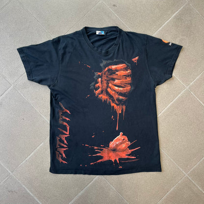 Mortal Kombat 9 Fatality Truck Tour 2011 Tee features a black T-shirt with a front graphic of a broken red ribcage and heart on a blood-covered surface. A vertical “Fatality” graphic is printed along the side, with Warner Bros. licensing text underneath the heart. One sleeve features the NetherRealm Studios logo. The back has the classic “Finish Him” text, Mortal Kombat logo, and matching licensing details.
