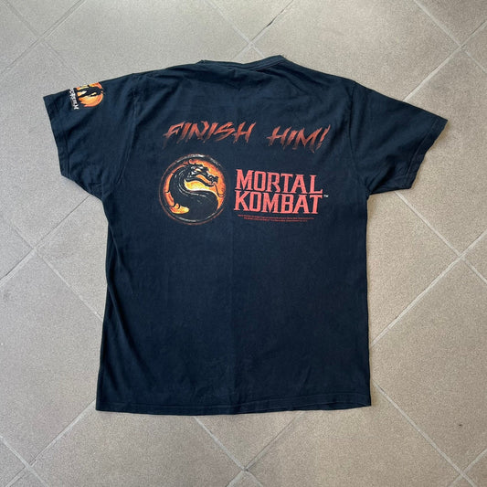 Mortal Kombat 9 Fatality Truck Tour 2011 Tee features a black T-shirt with a front graphic of a broken red ribcage and heart on a blood-covered surface. A vertical “Fatality” graphic is printed along the side, with Warner Bros. licensing text underneath the heart. One sleeve features the NetherRealm Studios logo. The back has the classic “Finish Him” text, Mortal Kombat logo, and matching licensing details.
