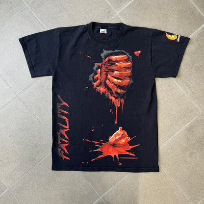 Mortal Kombat 9 Fatality Truck Tour 2011 Tee features a black T-shirt with a front graphic of a broken red ribcage and heart on a blood-covered surface. A vertical “Fatality” graphic is printed along the side, with Warner Bros. licensing text underneath the heart. One sleeve features the NetherRealm Studios logo. The back has the classic “Finish Him” text, Mortal Kombat logo, and matching licensing details.
