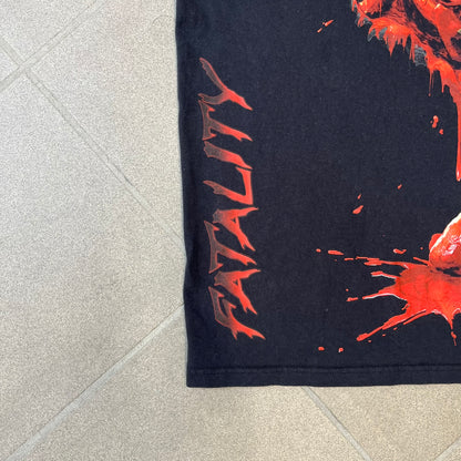 Mortal Kombat 9 Fatality Truck Tour 2011 Tee features a black T-shirt with a front graphic of a broken red ribcage and heart on a blood-covered surface. A vertical “Fatality” graphic is printed along the side, with Warner Bros. licensing text underneath the heart. One sleeve features the NetherRealm Studios logo. The back has the classic “Finish Him” text, Mortal Kombat logo, and matching licensing details.
