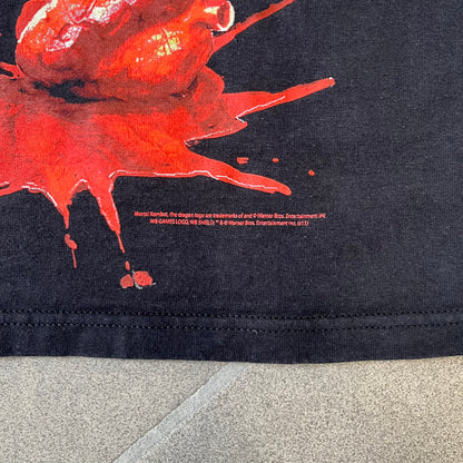 Mortal Kombat 9 Fatality Truck Tour 2011 Tee features a black T-shirt with a front graphic of a broken red ribcage and heart on a blood-covered surface. A vertical “Fatality” graphic is printed along the side, with Warner Bros. licensing text underneath the heart. One sleeve features the NetherRealm Studios logo. The back has the classic “Finish Him” text, Mortal Kombat logo, and matching licensing details.
