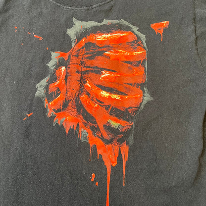 Mortal Kombat 9 Fatality Truck Tour 2011 Tee features a black T-shirt with a front graphic of a broken red ribcage and heart on a blood-covered surface. A vertical “Fatality” graphic is printed along the side, with Warner Bros. licensing text underneath the heart. One sleeve features the NetherRealm Studios logo. The back has the classic “Finish Him” text, Mortal Kombat logo, and matching licensing details.
