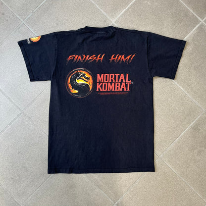 Mortal Kombat 9 Fatality Truck Tour 2011 Tee features a black T-shirt with a front graphic of a broken red ribcage and heart on a blood-covered surface. A vertical “Fatality” graphic is printed along the side, with Warner Bros. licensing text underneath the heart. One sleeve features the NetherRealm Studios logo. The back has the classic “Finish Him” text, Mortal Kombat logo, and matching licensing details.
