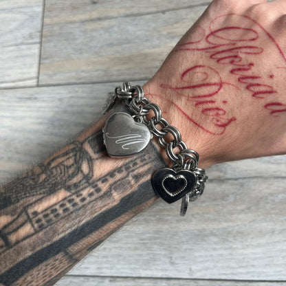 Moschino 2000s “Live Love Laugh” Charms Bracelet Watch is a stainless steel bracelet watch with a silver-tone finish. The bracelet is made of connected circular links and features multiple hanging heart-shaped charms. One charm displays “Live Love Laugh” text, while the main charm is a heart-shaped opening watch case with an “M” on the front. The watch dial is small and uses heart symbols in place of the main hour markers. All components are finished in silver tone.