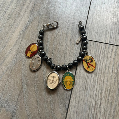 Moschino 2000’s “Time 4 Holy” Pendants Bracelet Watch is a bracelet watch from Moschino featuring a beaded construction with black pearly beads and multiple hanging religious-themed charms. The bracelet includes Madonna and holy figure pendants, with one charm functioning as a small hour-and-minute watch. Made in Italy in the early 2000s, the piece uses a pendant-style layout combining jewelry elements with a functional watch.