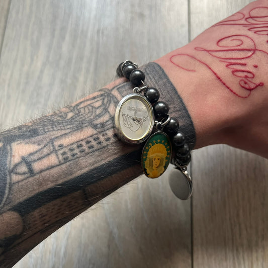 Moschino 2000’s “Time 4 Holy” Pendants Bracelet Watch is a bracelet watch from Moschino featuring a beaded construction with black pearly beads and multiple hanging religious-themed charms. The bracelet includes Madonna and holy figure pendants, with one charm functioning as a small hour-and-minute watch. Made in Italy in the early 2000s, the piece uses a pendant-style layout combining jewelry elements with a functional watch.