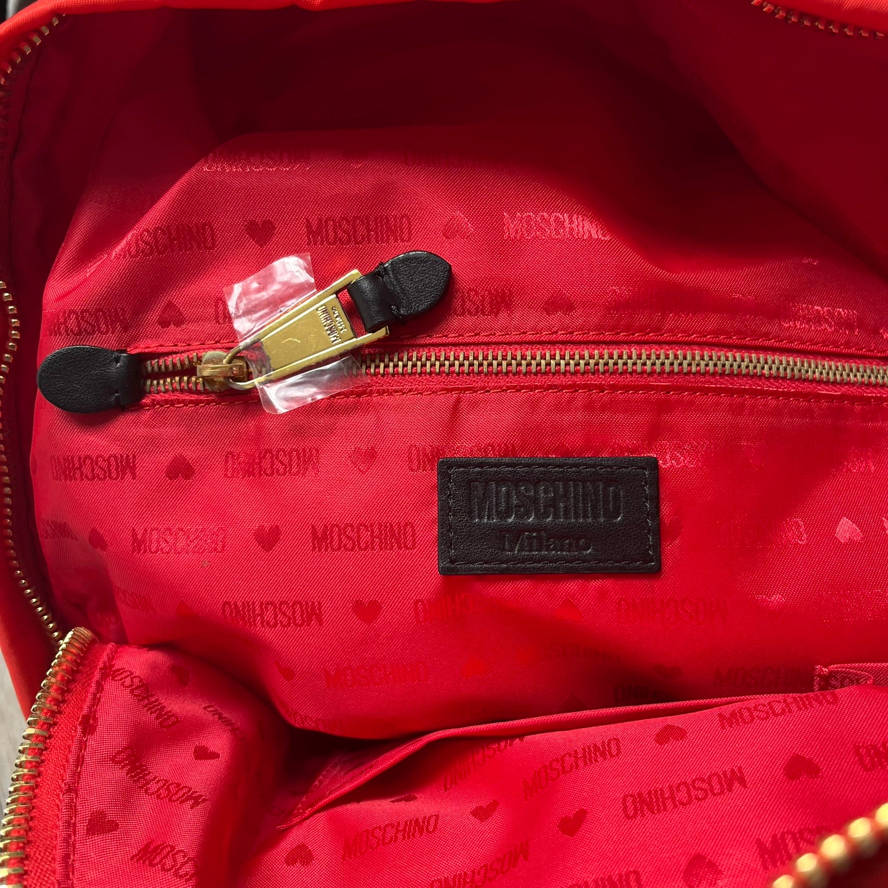 Moschino FW14 McDonald’s Fast Food Backpack is a red nylon backpack from the Autumn/Winter 2014 collection, designed by Jeremy Scott for his debut Moschino lineup. The front features yellow curved arches inspired by McDonald’s branding, with a front zip pocket printed with yellow Moschino text and black “Over 20 Billion Served” slogan. The bag includes gold-tone zippers with black leather pulls, black straps with Moschino logos, a branded interior lining, and comes with a Moschino dust bag. Made in Italy.